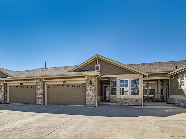 view of front of home with a garage, concrete driveway, a shingled roof, and stone siding