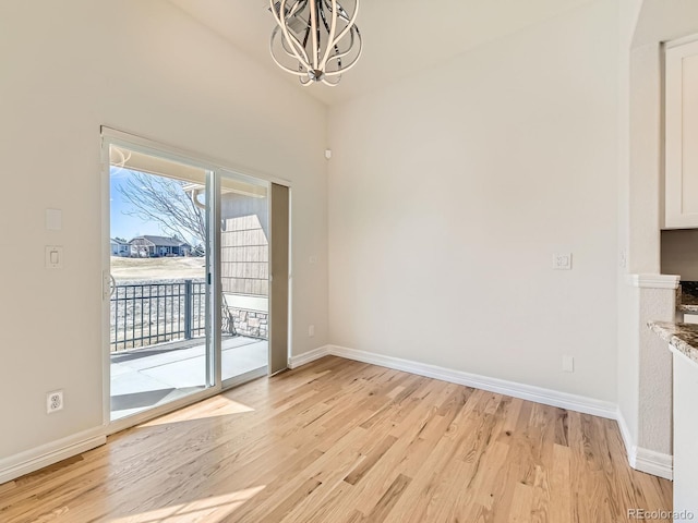 unfurnished dining area featuring light wood-type flooring, baseboards, vaulted ceiling, and a notable chandelier