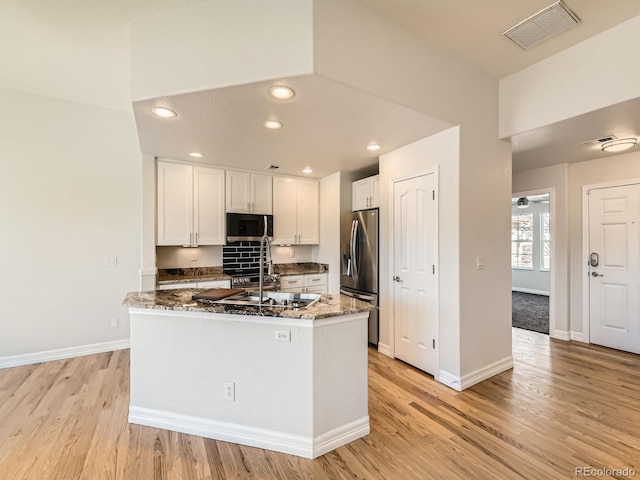 kitchen featuring stainless steel appliances, visible vents, white cabinets, dark stone countertops, and light wood-type flooring