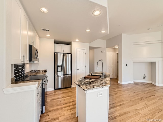 kitchen featuring visible vents, white cabinets, stainless steel appliances, light wood-style floors, and a sink