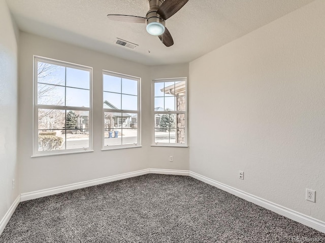 empty room featuring dark colored carpet, a wealth of natural light, visible vents, and baseboards