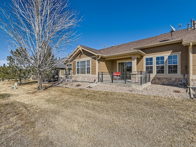 back of house featuring stone siding, a patio area, a lawn, and roof with shingles