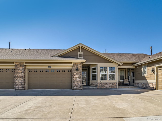 view of front of property with an attached garage, stone siding, roof with shingles, and concrete driveway