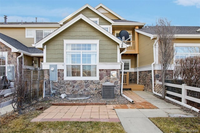 rear view of property featuring stone siding, a balcony, central AC, and fence