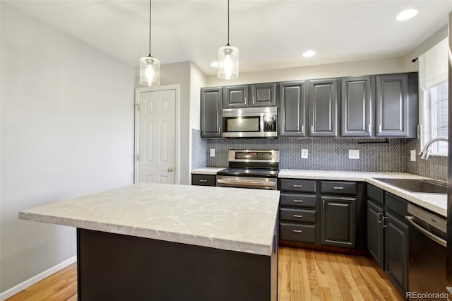 kitchen with a sink, hanging light fixtures, stainless steel appliances, tasteful backsplash, and light wood-type flooring