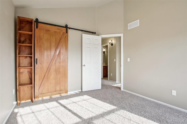 unfurnished bedroom with visible vents, lofted ceiling, a barn door, carpet flooring, and baseboards