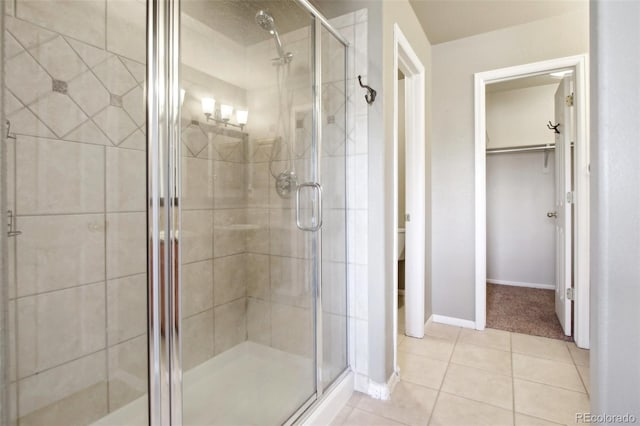 bathroom featuring tile patterned flooring, a shower stall, a walk in closet, and baseboards