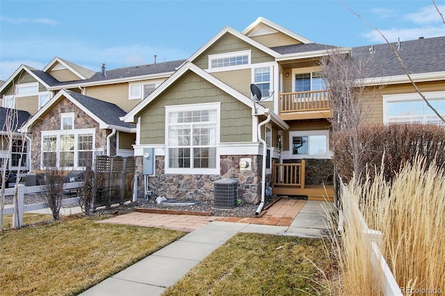 rear view of house featuring fence, central AC unit, a shingled roof, stone siding, and a lawn