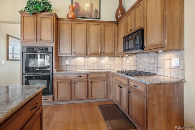 kitchen with decorative backsplash, light stone countertops, stainless steel appliances, and light wood-type flooring