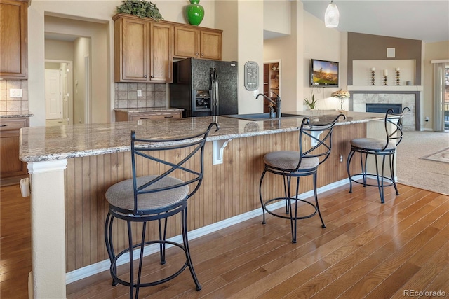 kitchen featuring decorative backsplash, light wood-type flooring, black fridge with ice dispenser, vaulted ceiling, and a breakfast bar area