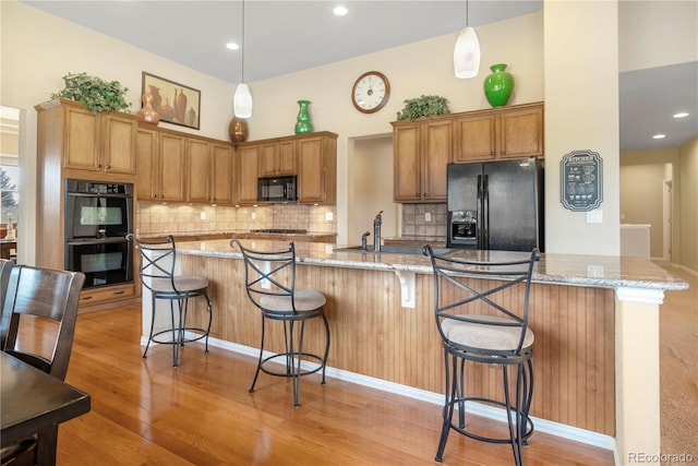 kitchen featuring light stone countertops, pendant lighting, light hardwood / wood-style floors, a kitchen bar, and black appliances