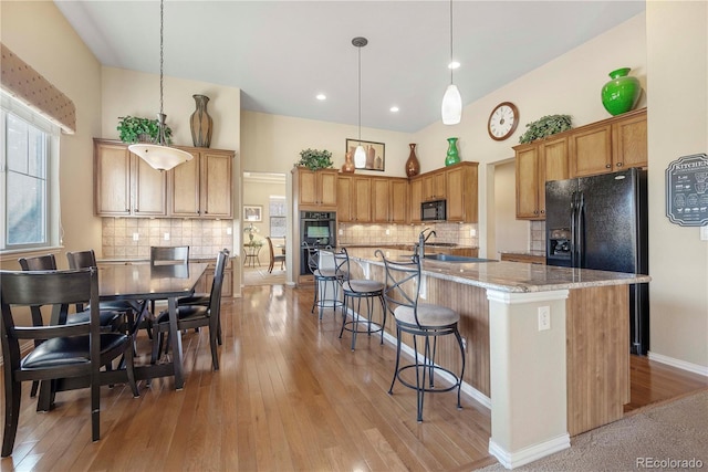 kitchen featuring light stone countertops, an island with sink, pendant lighting, light hardwood / wood-style floors, and black appliances