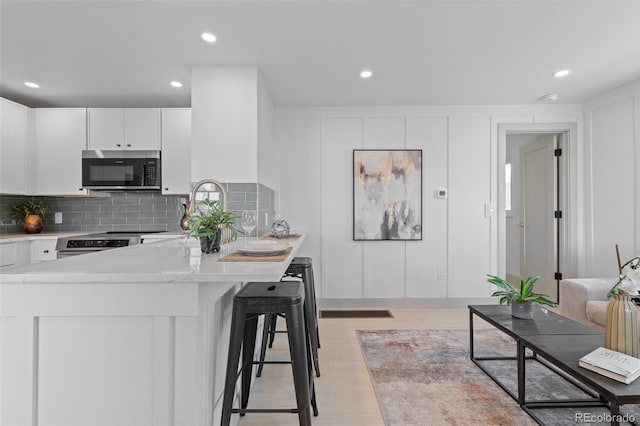 kitchen featuring tasteful backsplash, white cabinets, a kitchen bar, light stone counters, and stainless steel appliances