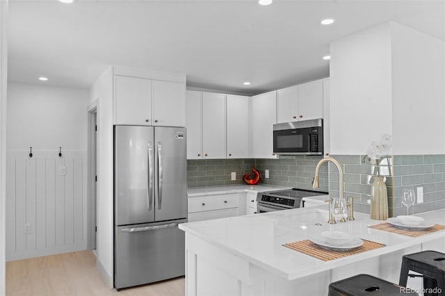 kitchen with appliances with stainless steel finishes, a breakfast bar, white cabinetry, kitchen peninsula, and light wood-type flooring