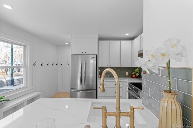 kitchen featuring light stone counters, appliances with stainless steel finishes, backsplash, and white cabinets