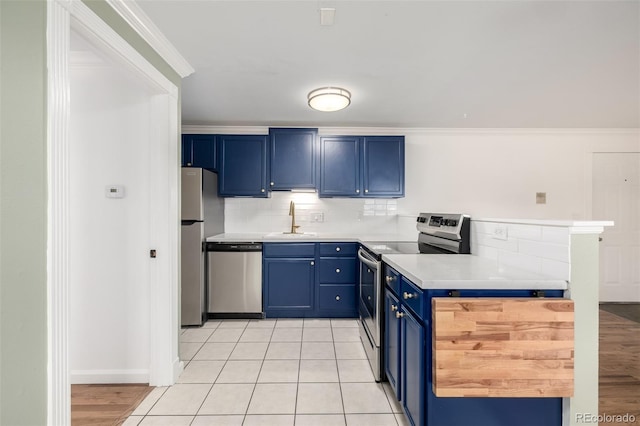 kitchen with a sink, blue cabinetry, stainless steel appliances, a peninsula, and tasteful backsplash