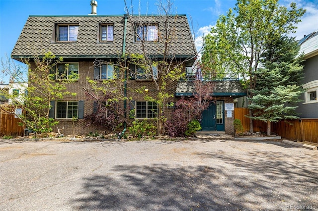 exterior space featuring brick siding, mansard roof, fence, and roof with shingles