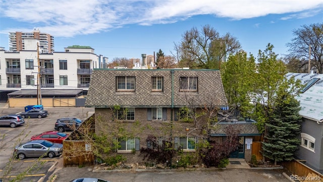exterior space with a shingled roof, mansard roof, uncovered parking, and brick siding