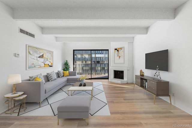 living room featuring beamed ceiling, light wood-type flooring, and a textured ceiling