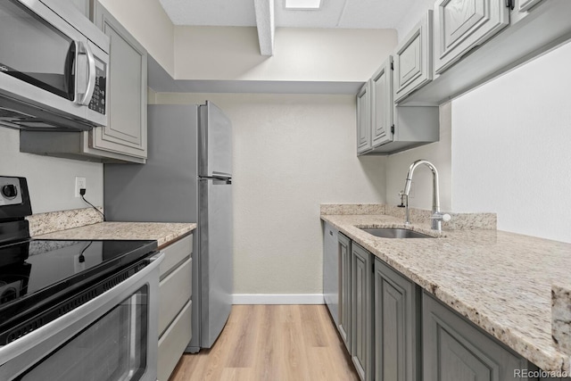 kitchen featuring appliances with stainless steel finishes, light wood-type flooring, gray cabinetry, and sink