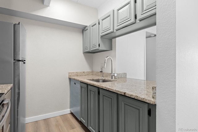 kitchen with sink, gray cabinets, light wood-type flooring, light stone counters, and stainless steel appliances