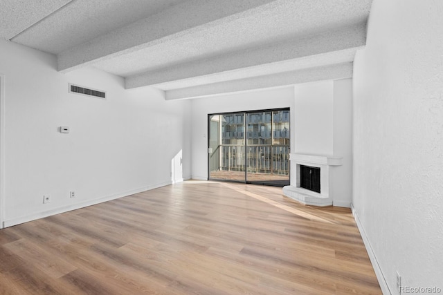 unfurnished living room featuring a textured ceiling, beam ceiling, wood-type flooring, and a fireplace