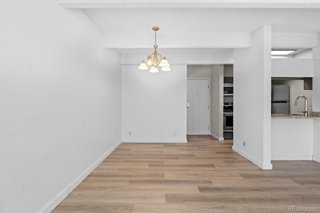 unfurnished dining area featuring sink, light wood-type flooring, a textured ceiling, and an inviting chandelier