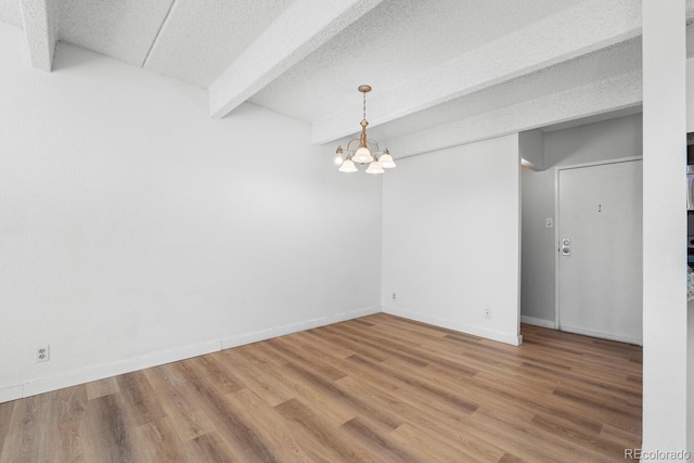 spare room featuring a chandelier, wood-type flooring, a textured ceiling, and beamed ceiling