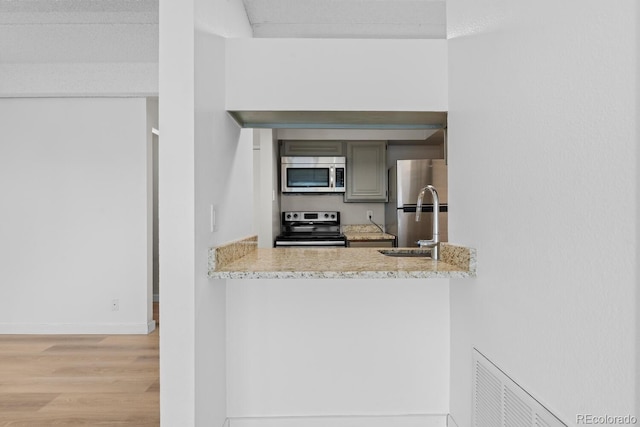 kitchen with light stone countertops, stainless steel appliances, gray cabinets, and light hardwood / wood-style floors