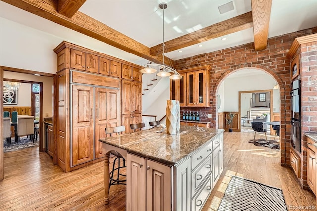 kitchen featuring stone counters, arched walkways, a kitchen bar, beamed ceiling, and light wood-type flooring