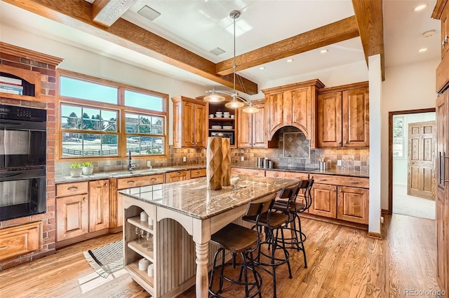 kitchen with light stone countertops, a kitchen island, open shelves, black appliances, and beamed ceiling