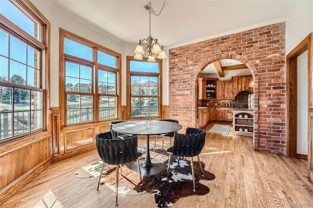 dining room featuring wainscoting, crown molding, light wood-style floors, and an inviting chandelier