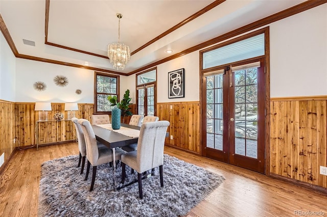 dining area featuring a wainscoted wall, a raised ceiling, wood walls, and french doors