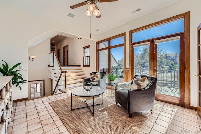 living area featuring stairway, baseboards, visible vents, and a ceiling fan