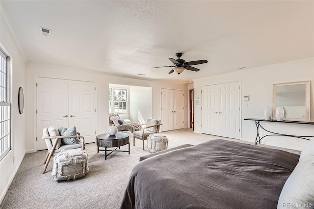 bedroom featuring light colored carpet, two closets, visible vents, and crown molding