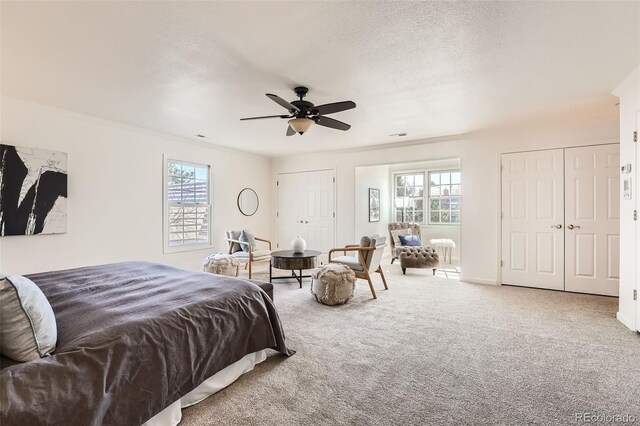 carpeted bedroom with multiple windows, multiple closets, a textured ceiling, and a ceiling fan