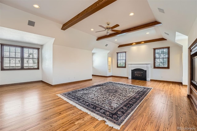 living area featuring baseboards, light wood-style flooring, a fireplace, ceiling fan, and beamed ceiling