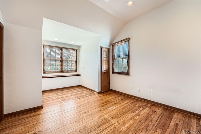 empty room with baseboards, vaulted ceiling, and light wood finished floors