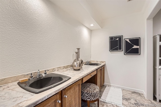 bathroom with double vanity, a textured wall, baseboards, and a sink