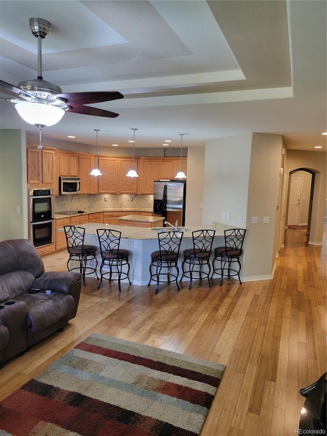 kitchen featuring a breakfast bar area, light wood-type flooring, a tray ceiling, stainless steel appliances, and backsplash