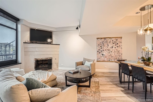 living area with a tile fireplace, baseboards, and wood finished floors