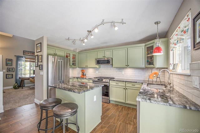9200 W Indore Dr, Littleton, CO 80128 - kitchen featuring appliances with stainless steel finishes, green cabinets, a kitchen bar, a kitchen island, and backsplash