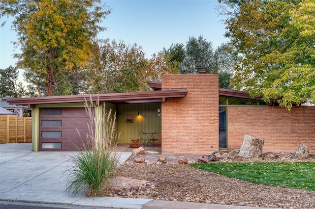 view of front of house featuring a chimney, concrete driveway, a garage, and fence