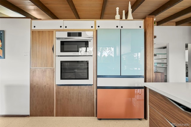 5450 Mohawk Rd, Littleton, CO 80123 - kitchen featuring freestanding refrigerator, double oven, dark aggregate flooring, beamed ceiling, and white cabinetry
