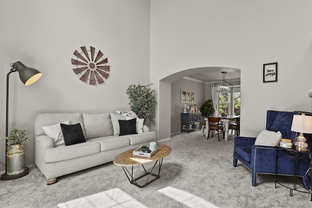 carpeted living room featuring crown molding, a high ceiling, and a notable chandelier