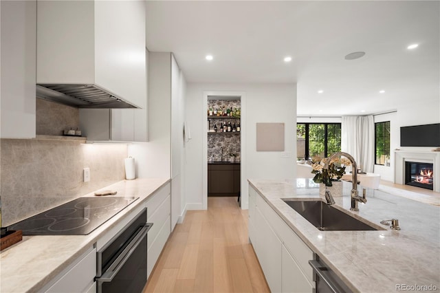 332 S Franklin St, Denver, CO 80209 - kitchen featuring oven, black electric stovetop, premium range hood, light wood finished floors, and white cabinetry