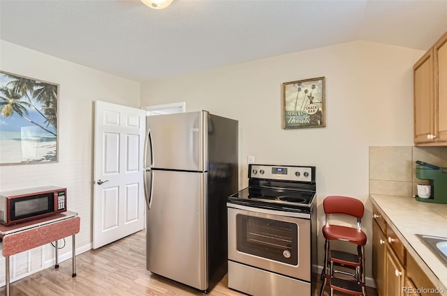 kitchen with light hardwood / wood-style flooring, stainless steel appliances, light brown cabinetry, and backsplash