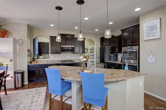 kitchen with sink, stainless steel appliances, decorative light fixtures, and an island with sink