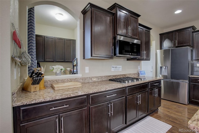 kitchen featuring stainless steel appliances, light stone countertops, dark brown cabinetry, and dark hardwood / wood-style flooring