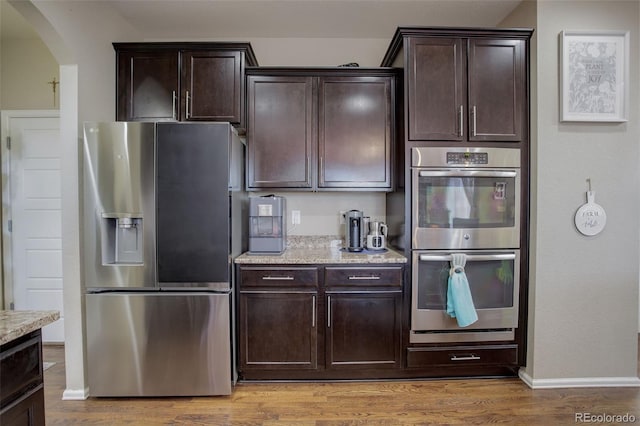 kitchen with appliances with stainless steel finishes, dark brown cabinets, and light wood-type flooring